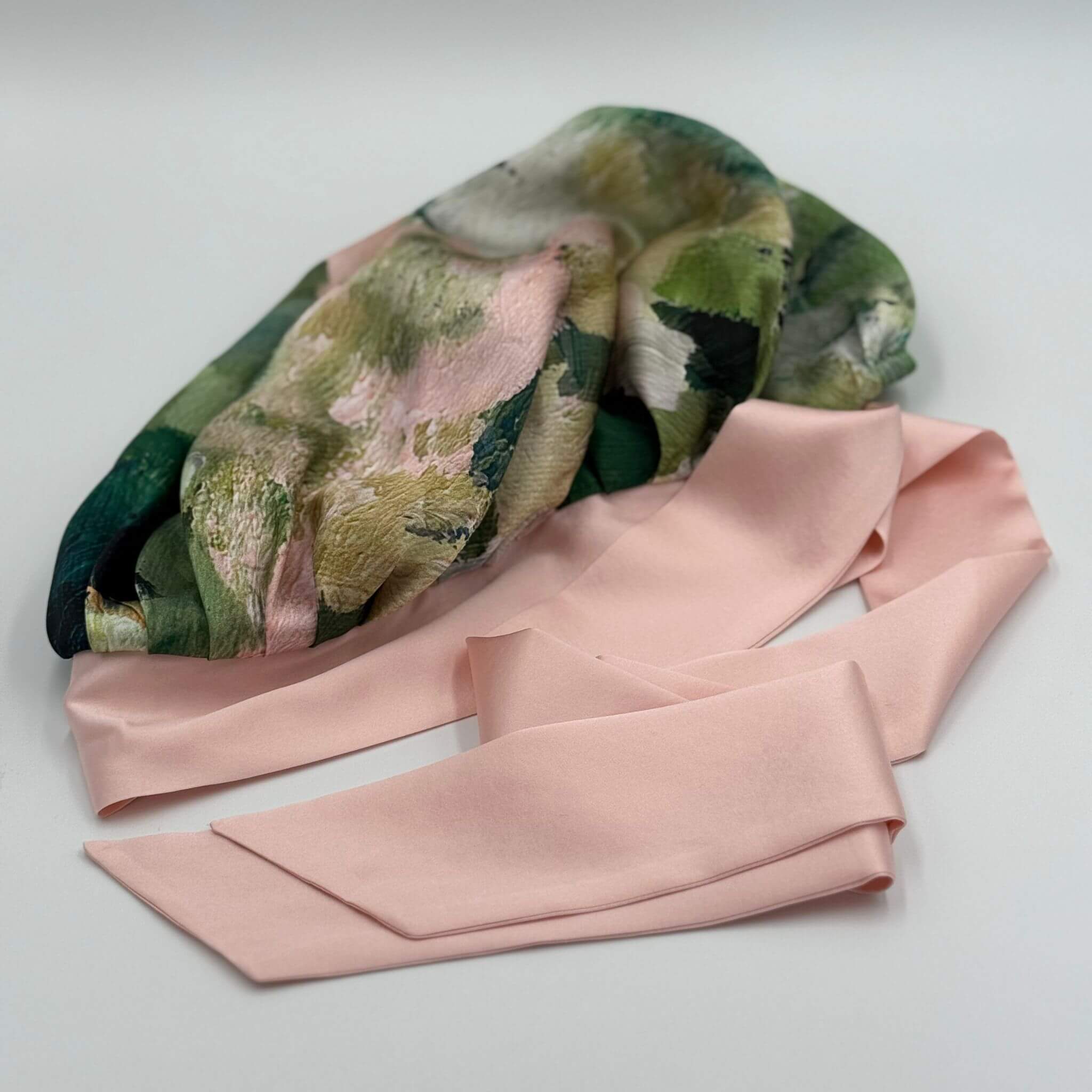 Folded pink silk bonnet with a green and pink pattern on a light gray background