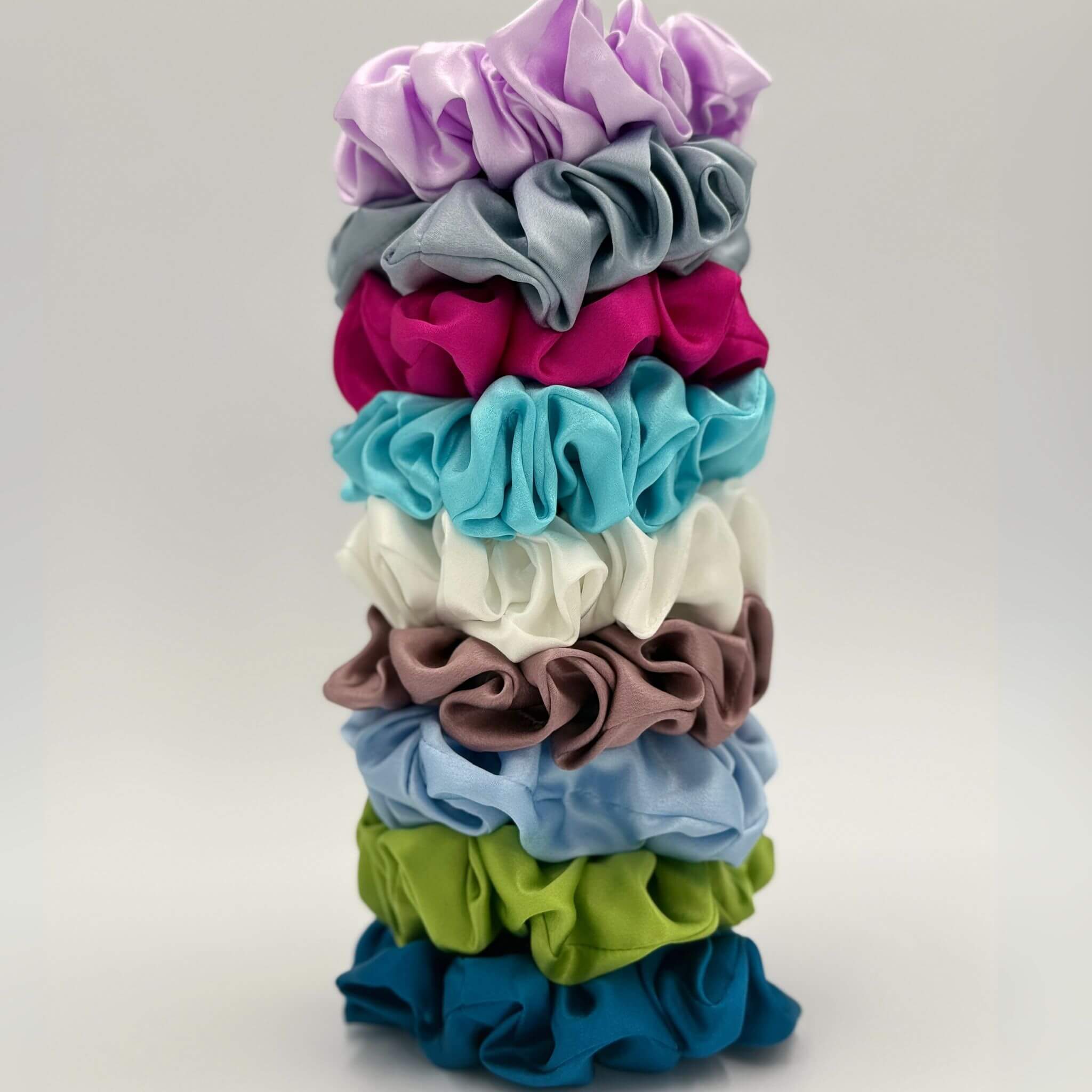 Stack of colorful silk scrunchies on a light gray background