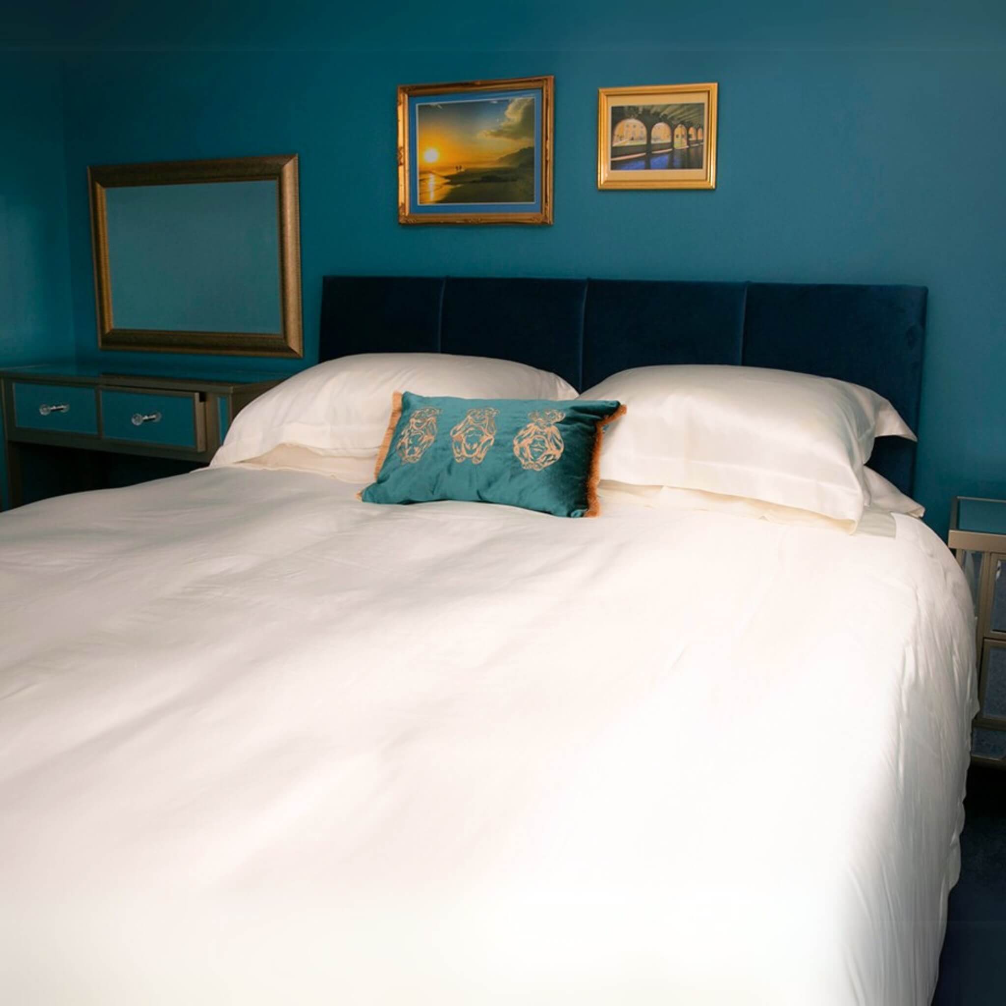 Bedroom with an ivory silk bed, pillows, and framed pictures on a blue wall.
