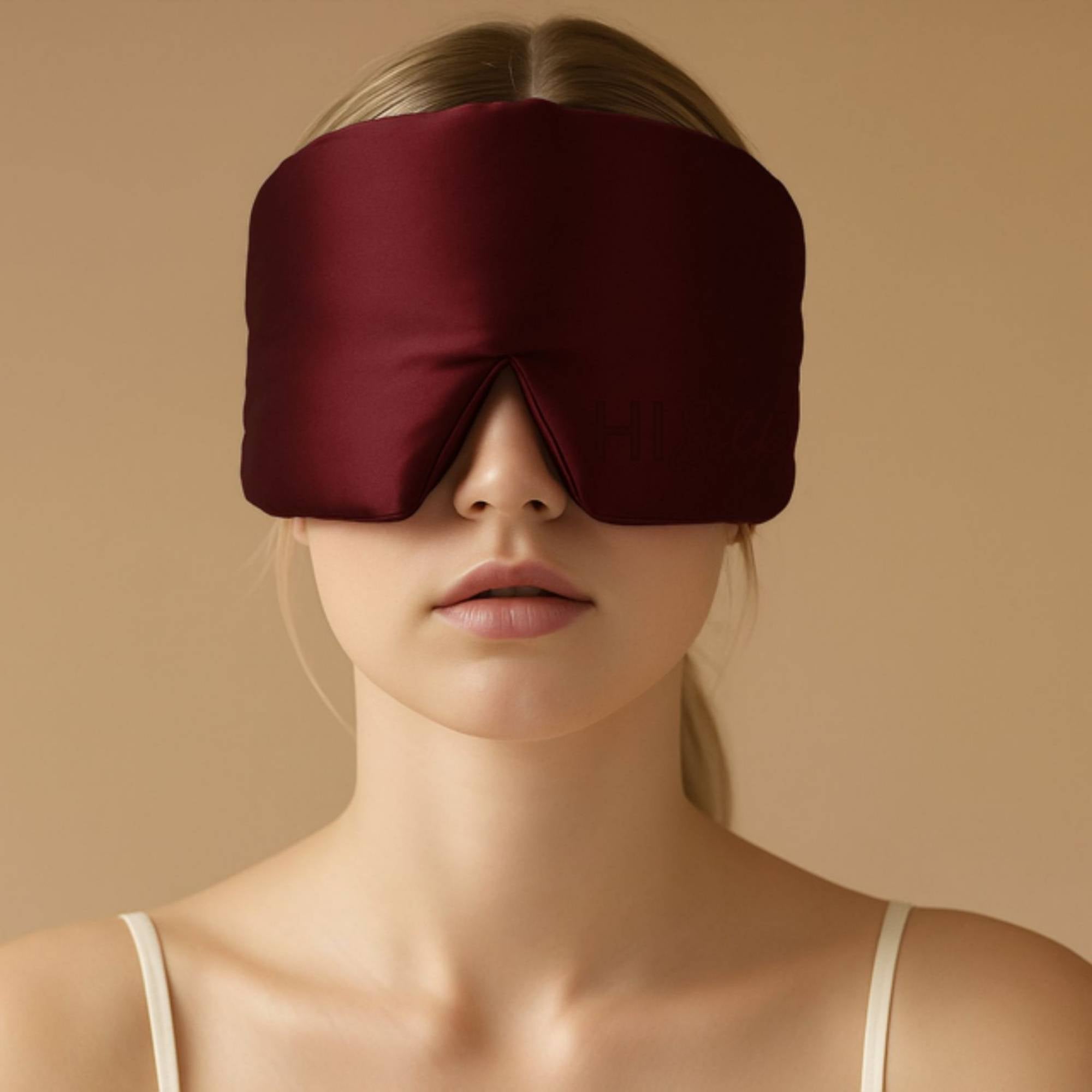 Woman wearing a burgundy 3d silk sleep mask against a beige background