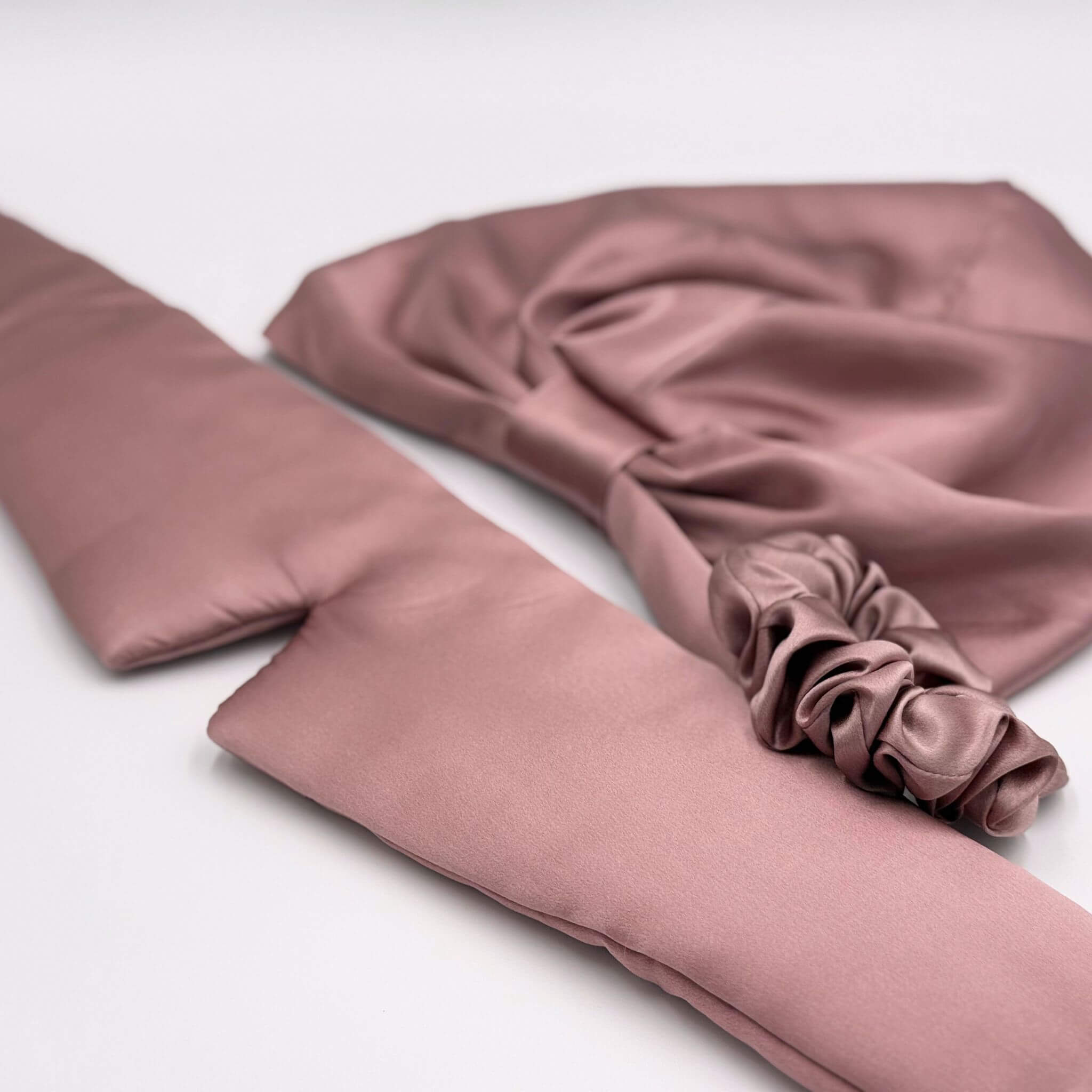 pink silk eye mask, bonnet and scrunchie on a white background