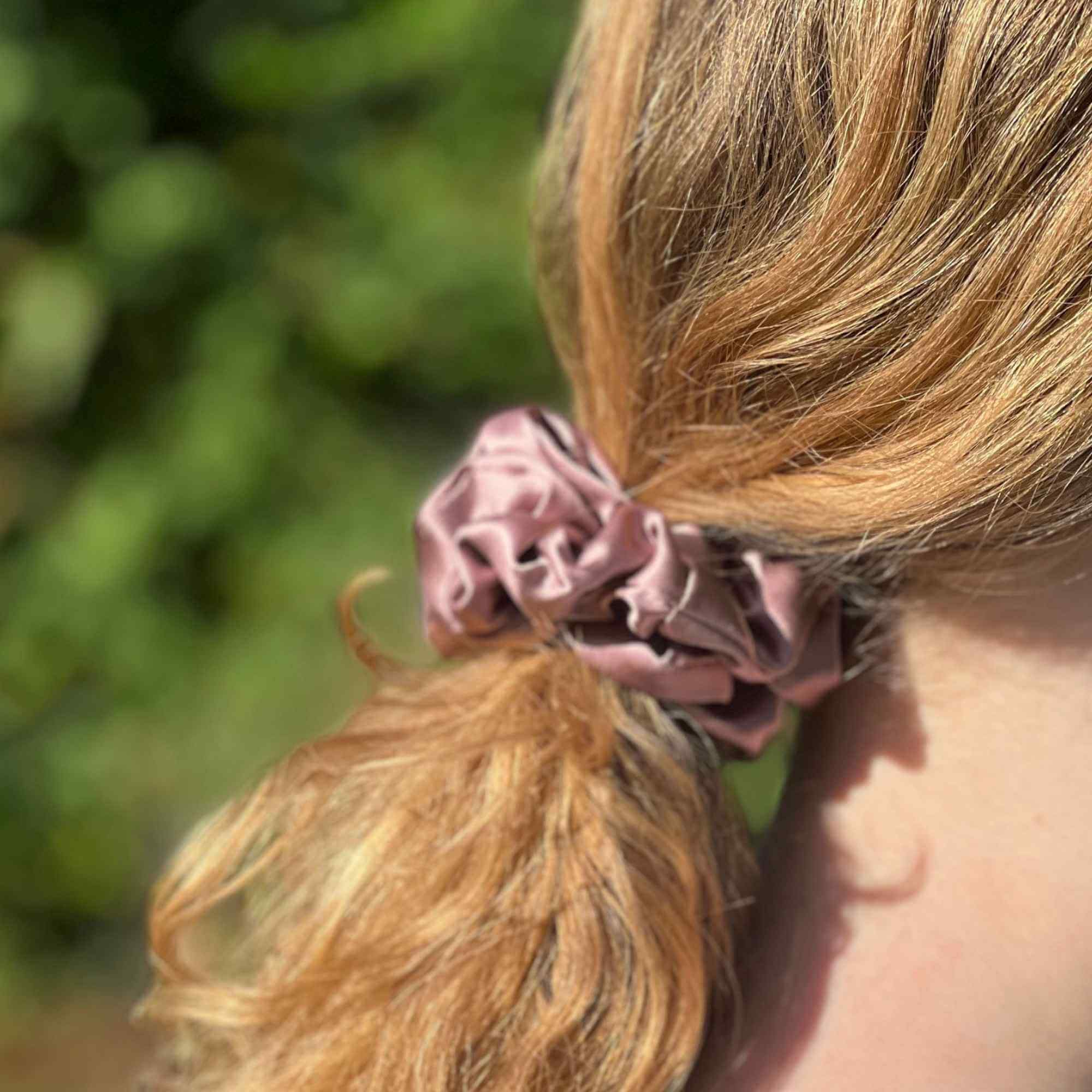dusty Pink mulberry silk scrunchie in a person's hair with a blurred green background