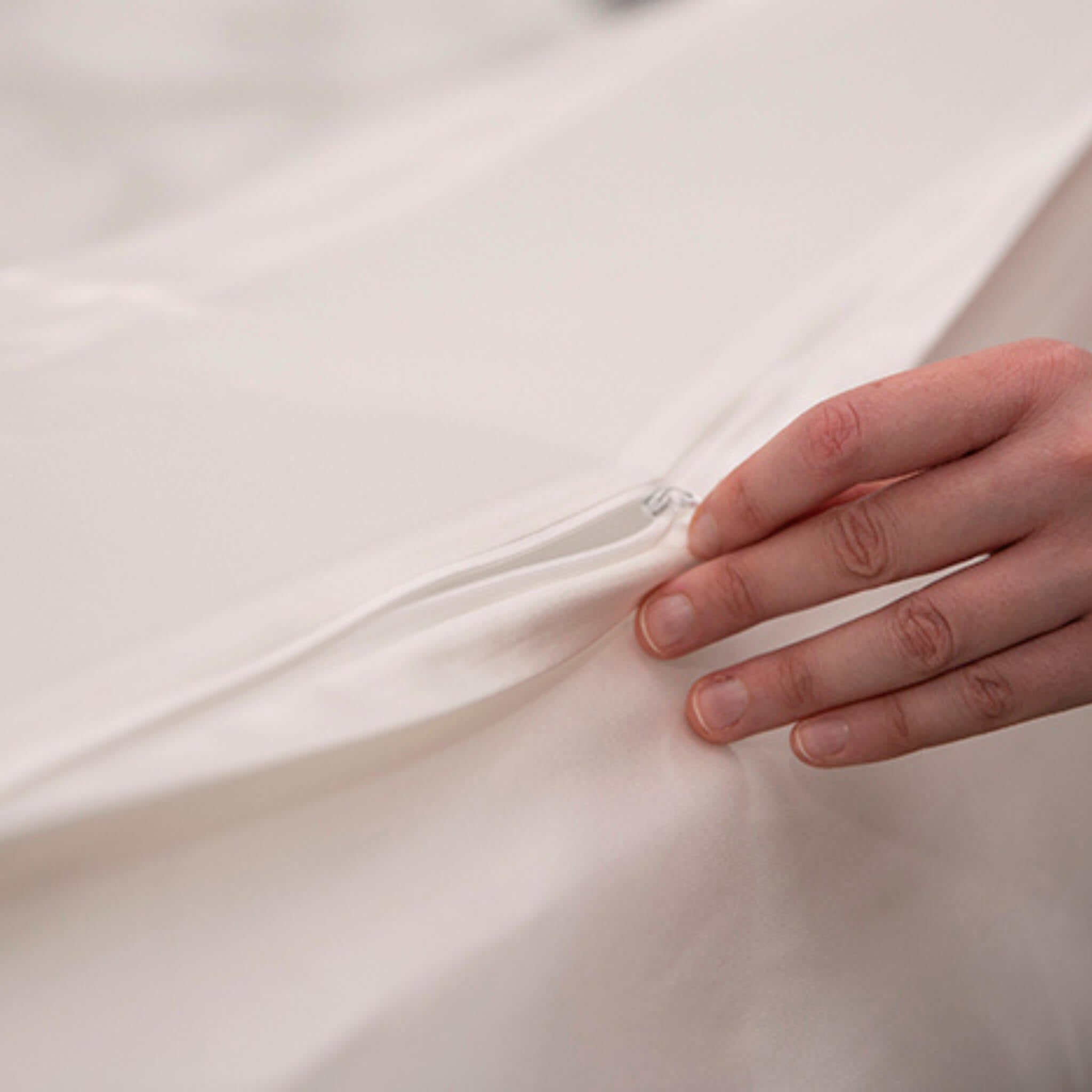 Close-up of a hand touching a smooth, ivory silk fabric surface with a concealed zip