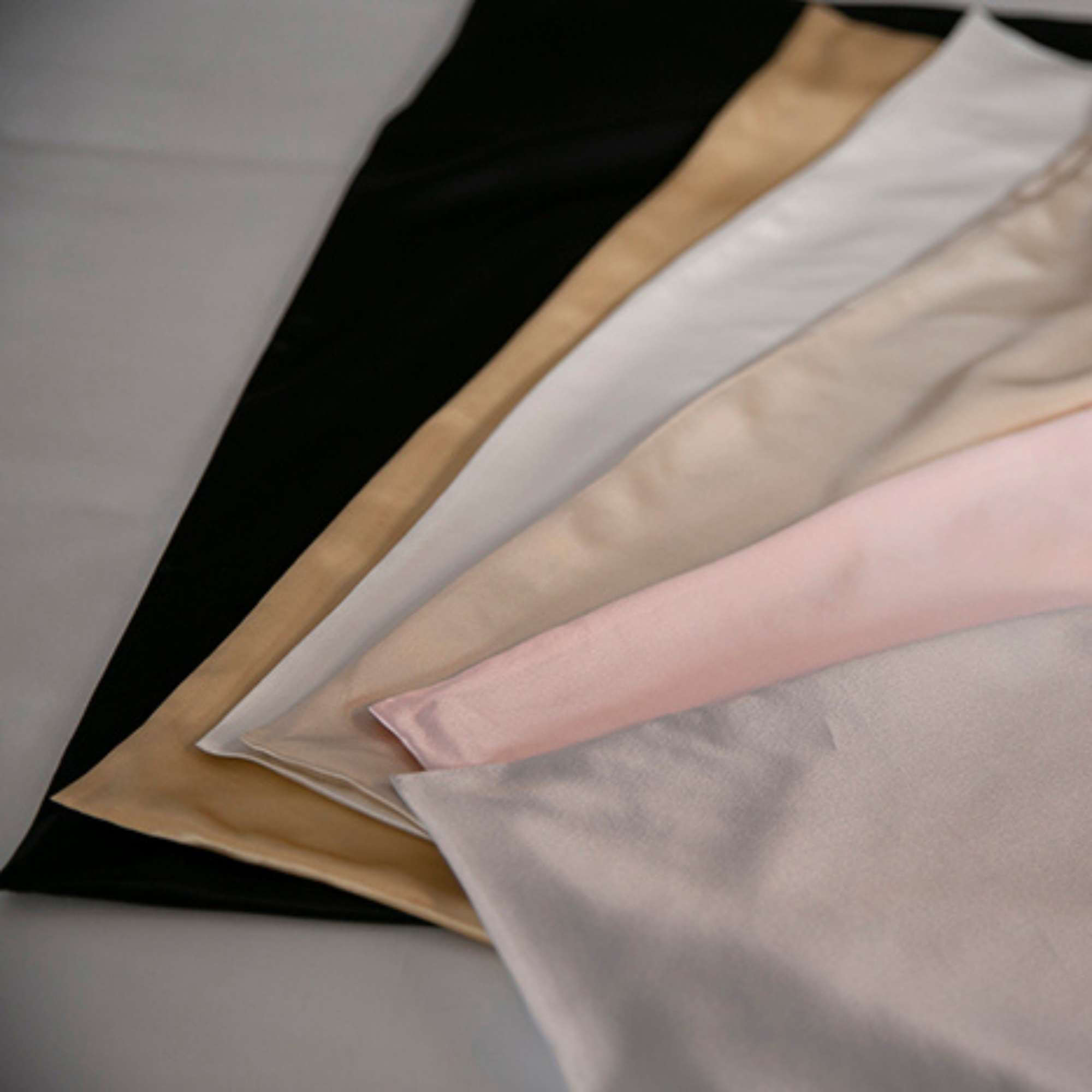 Collection of silk pillowcases in various colors on a neutral background