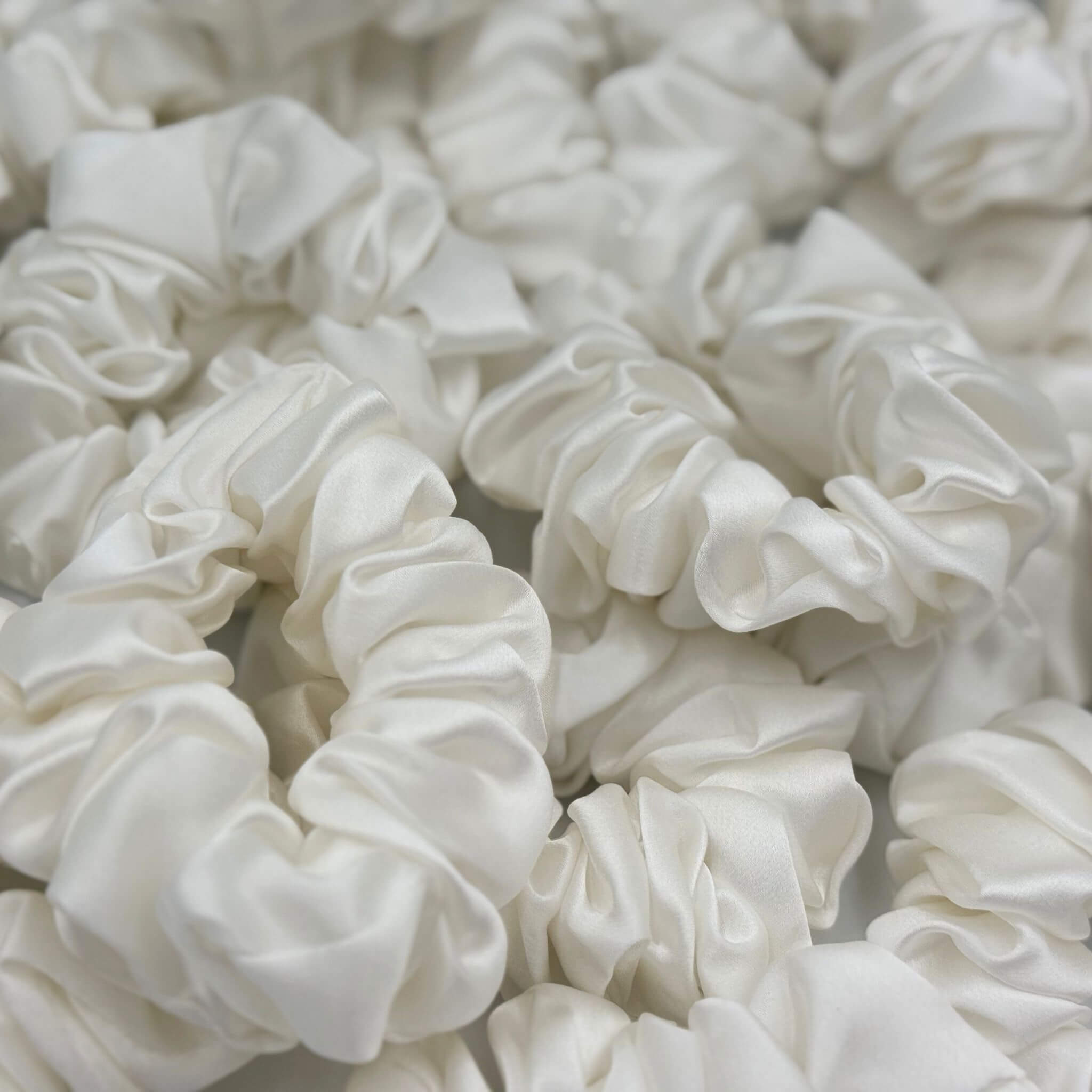Close-up of multiple white silk scrunchies on a light background