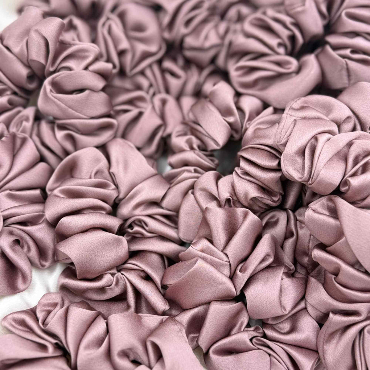 Close-up of multiple dusty pink mulberry silk scrunchies stacked together