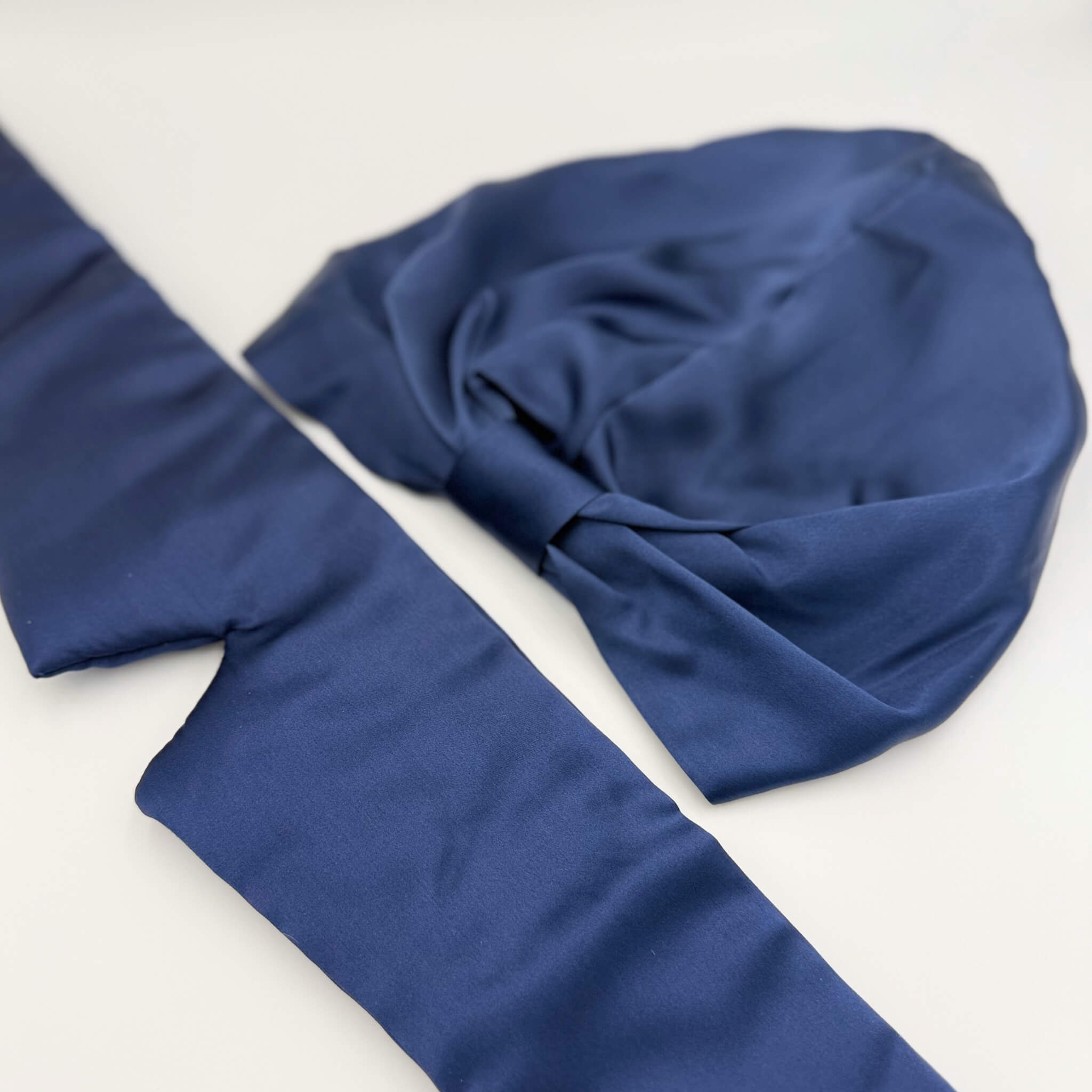 Navy blue silk bonnet and eye mask set lying flat on a white background