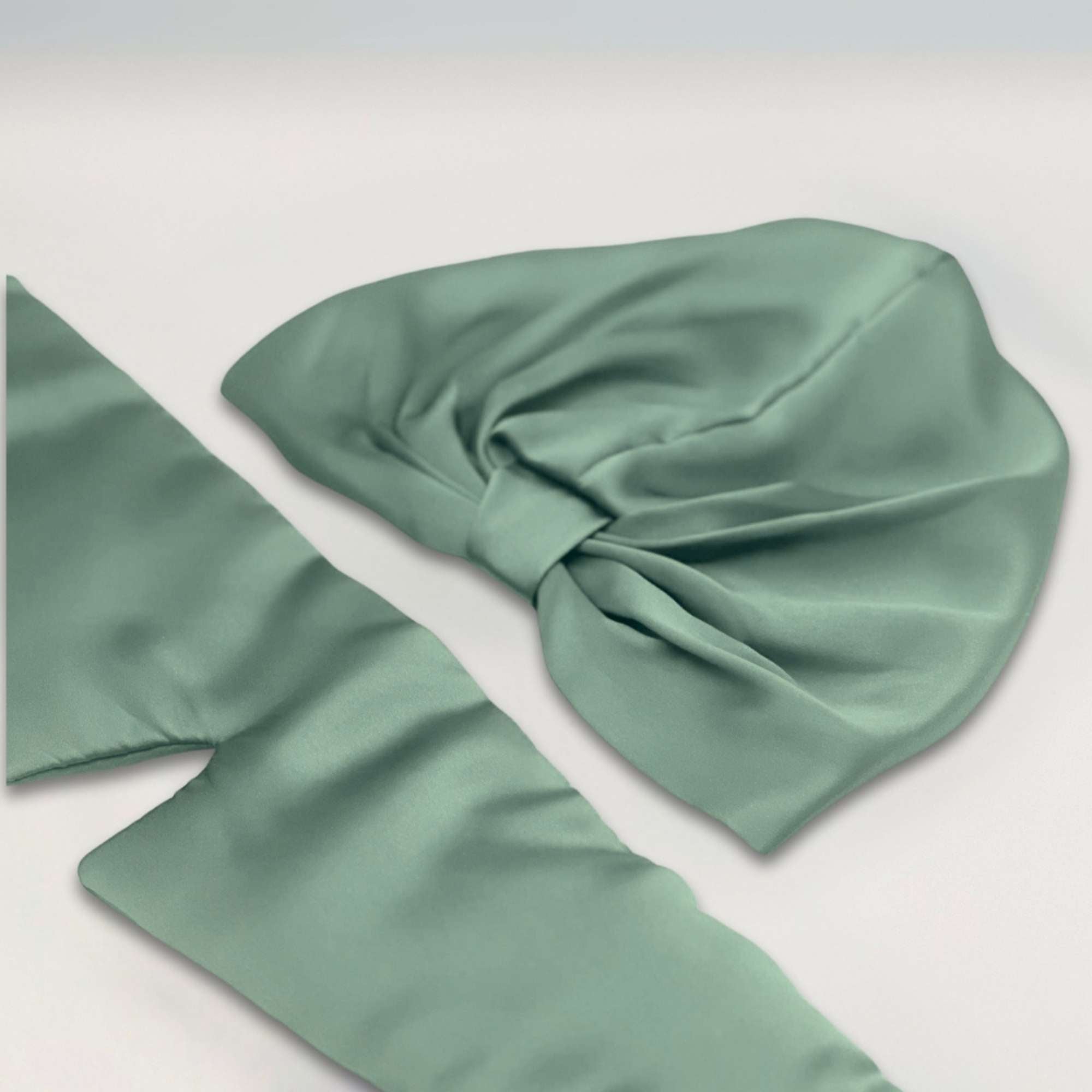 Green silk bonnet and eye mask set lying flat on a white background