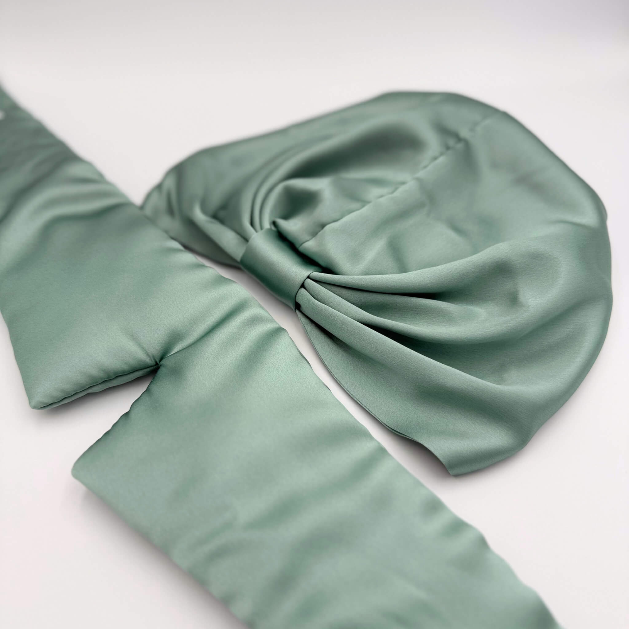 Green silk bonnet and eye mask set lying flat on a white background