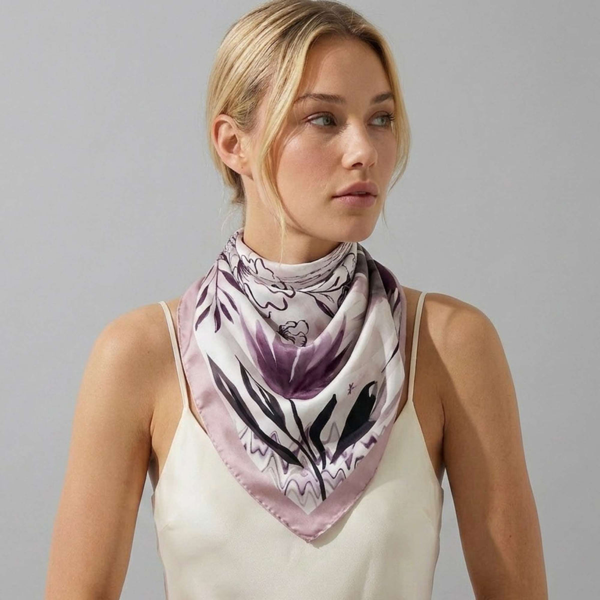 Woman wearing a petals and palms silk twill scarf on a plain background