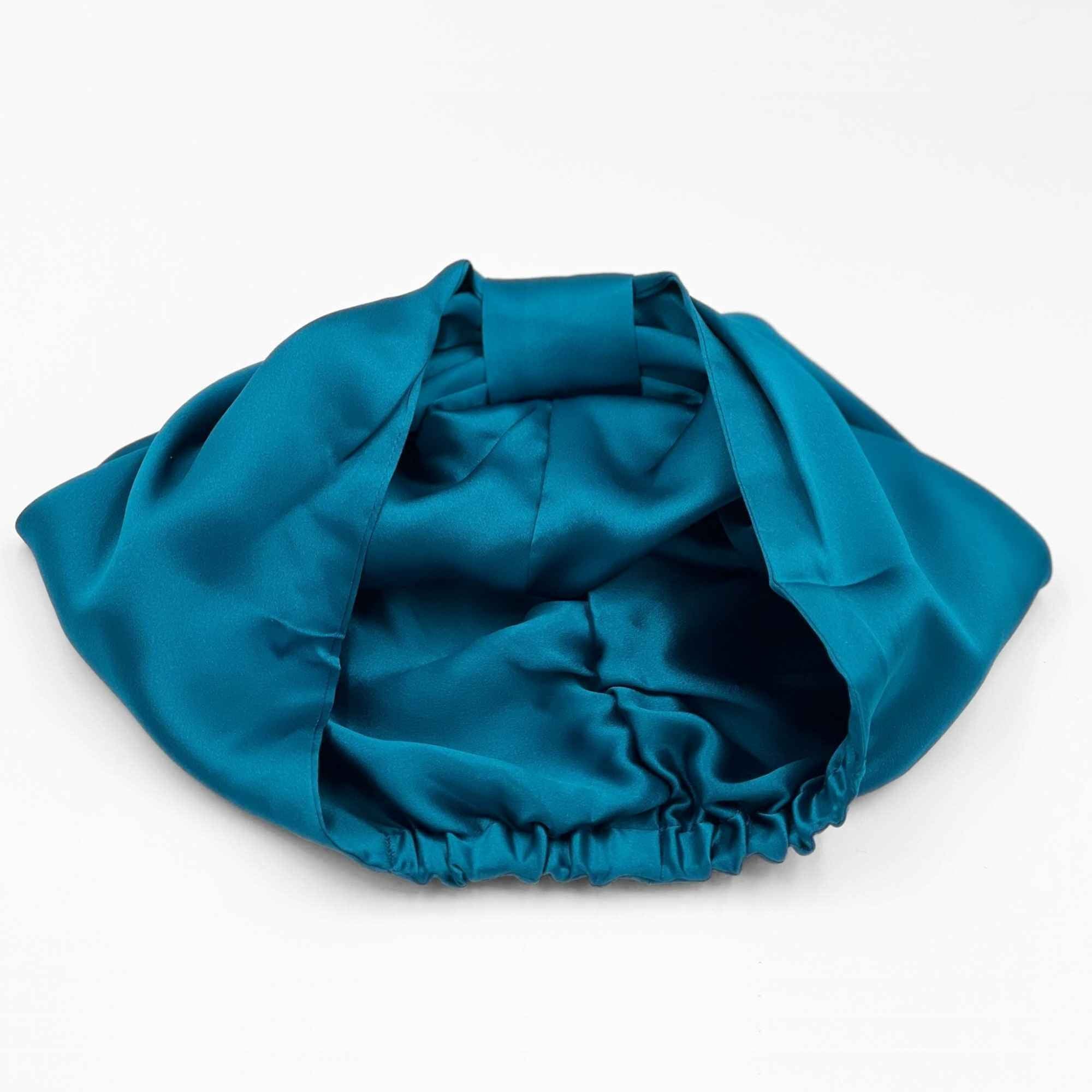 Teal bonnet laying flat, showing it's reversible quality, line with silk