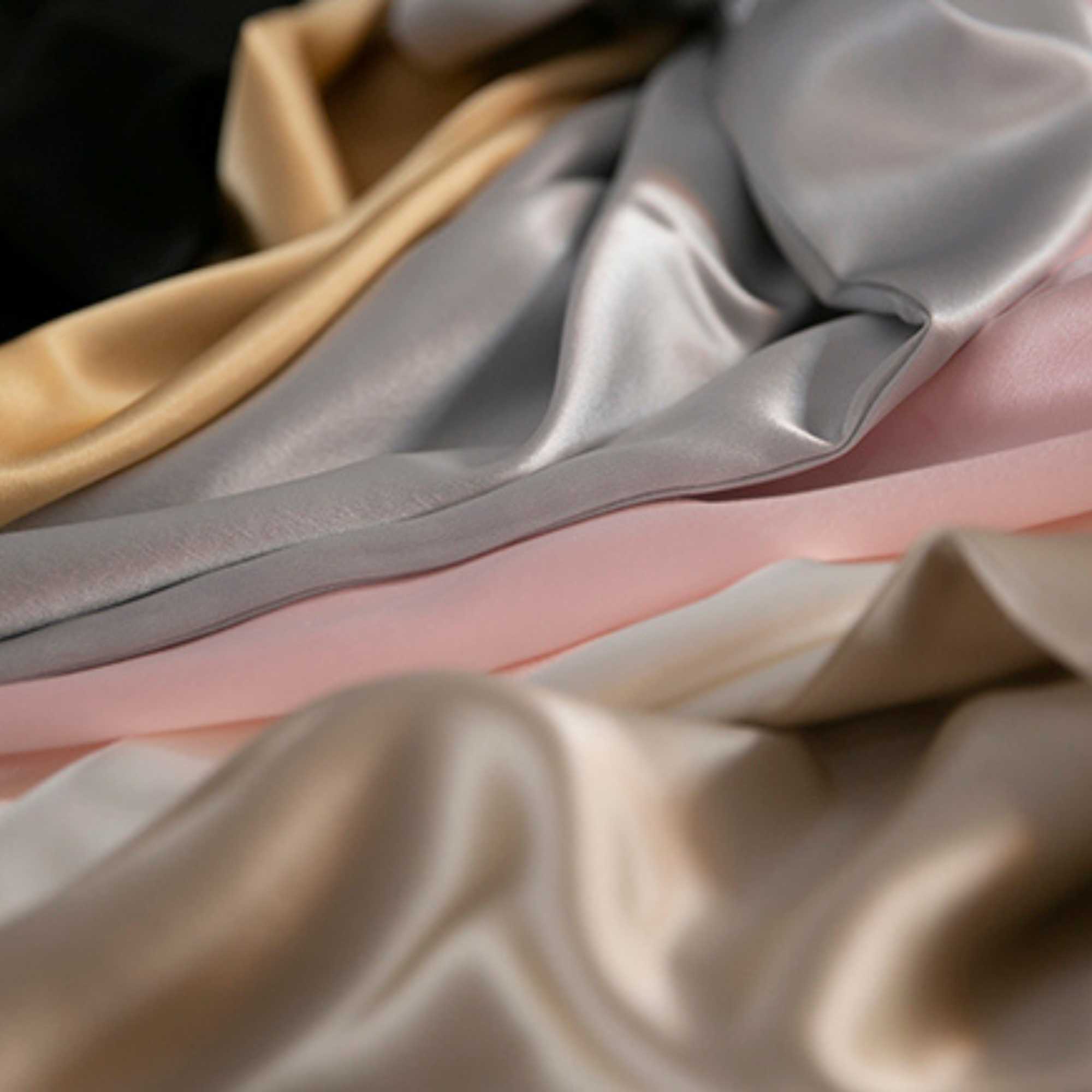 Close-up of silk pillowcases in various colors including champagne, gray, and pink.