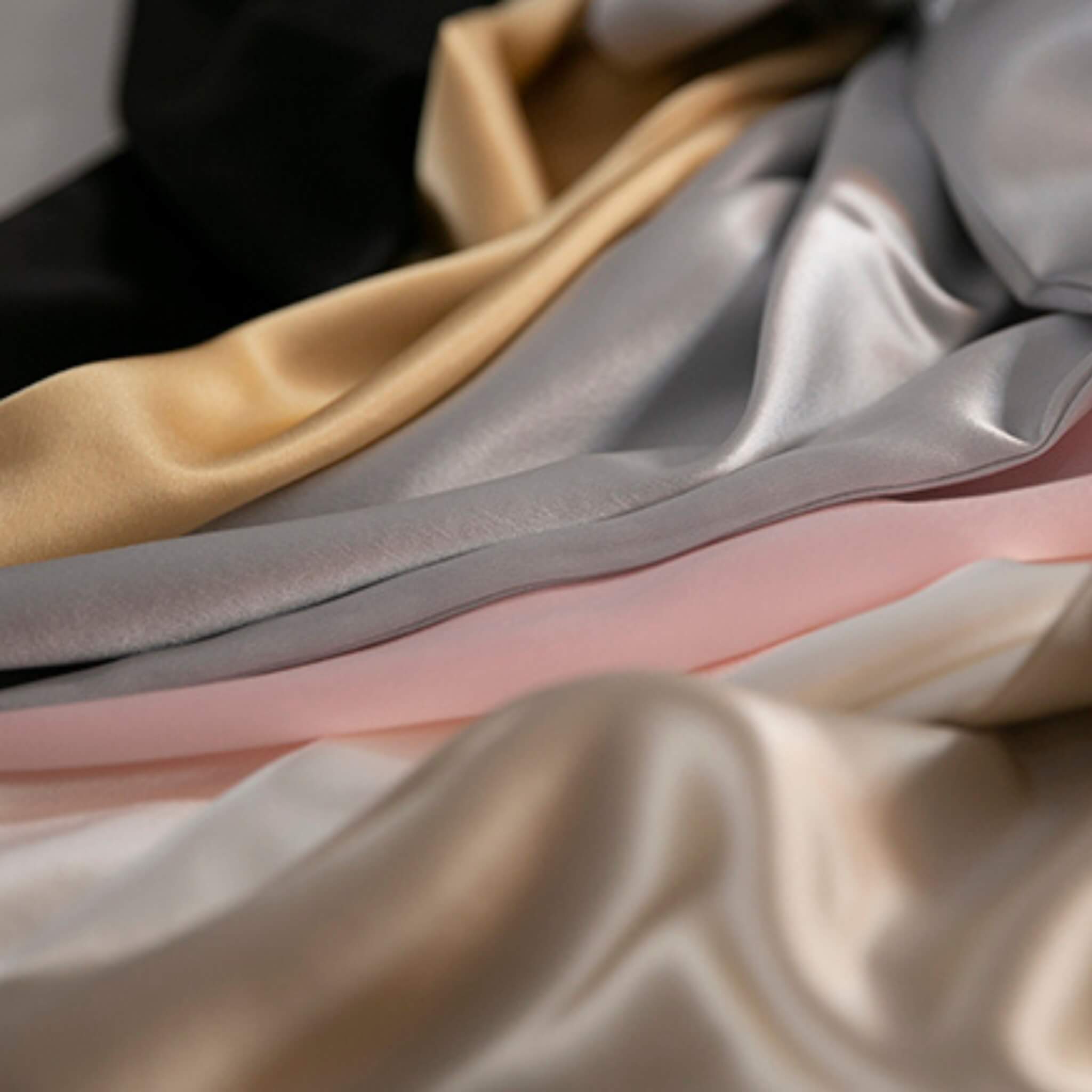 Close-up of silk pillowcases in various colors including champagne, gray, and pink.