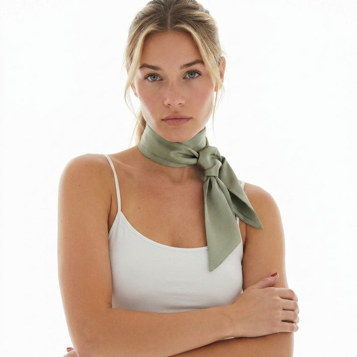 Woman wearing a sage green silk skinny scarf around her neck on a white background