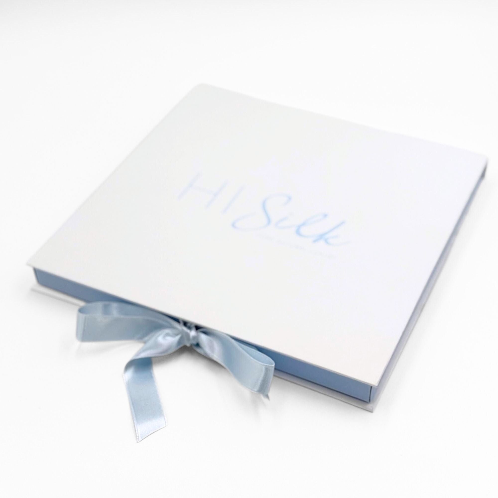 White silk scarf box with a blue ribbon and blue writing on saying HI Silk on a white background