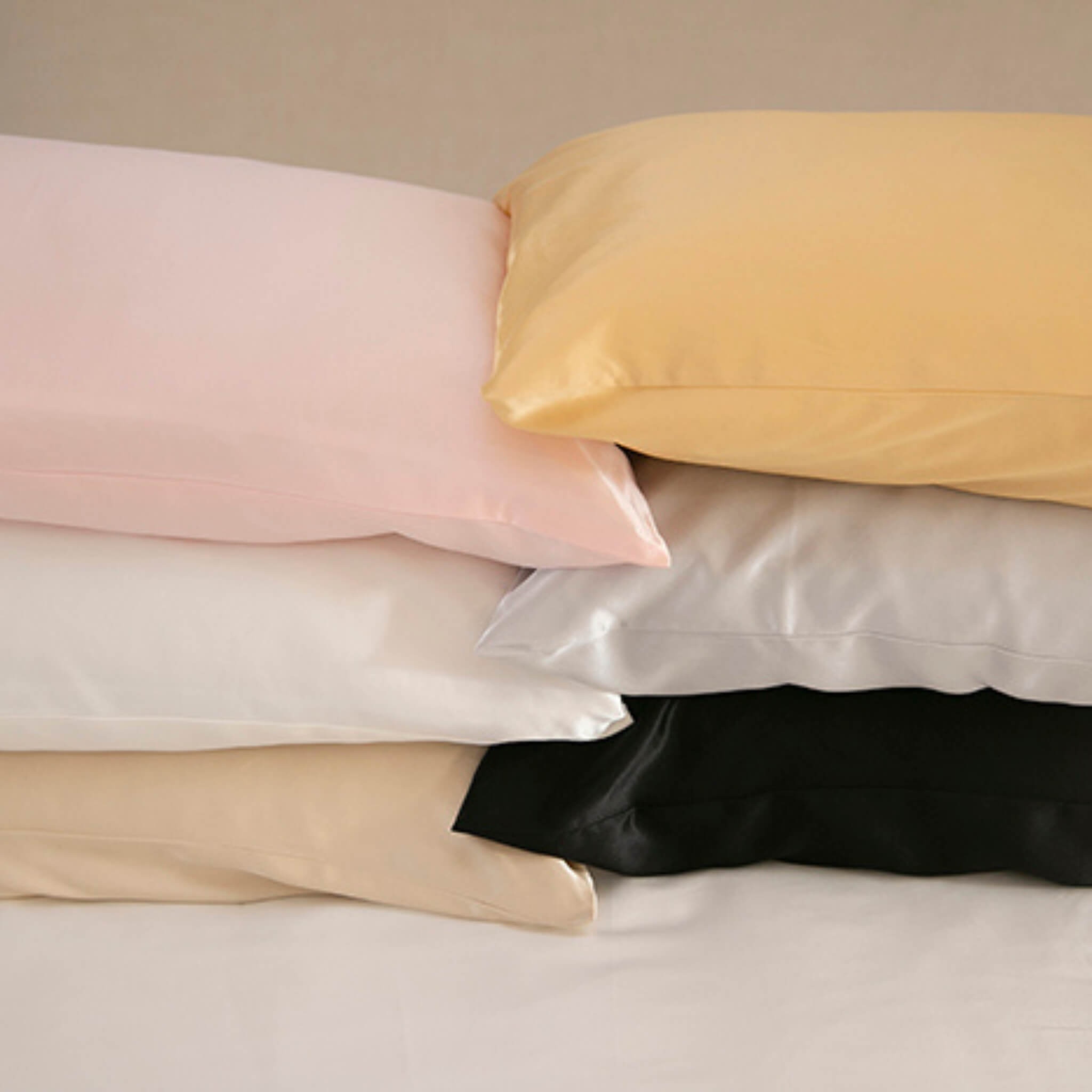 Stack of silk pillows in various colors on a neutral background