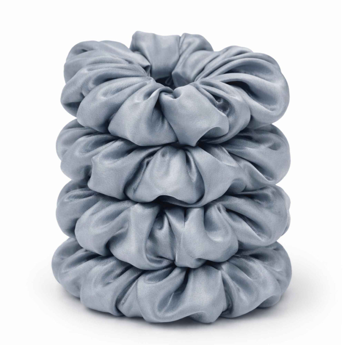 Stack of four dusty blue silk scrunchies on a white background