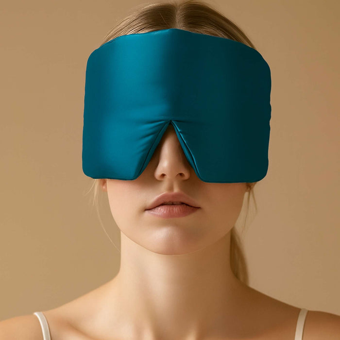 Person wearing a teal silk sleep mask against a beige background