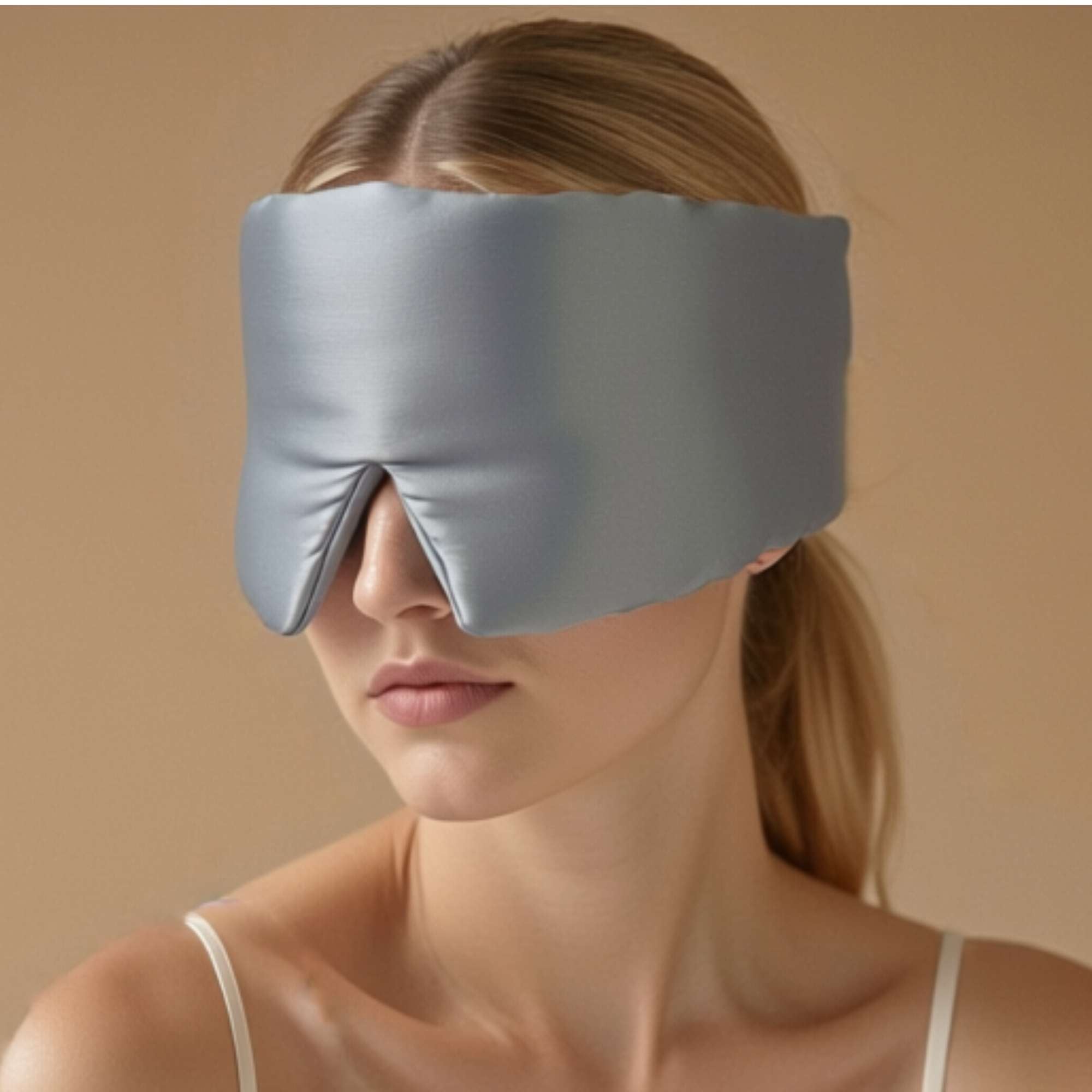 Woman wearing a pale blue mulberry silk eye mask against a beige background