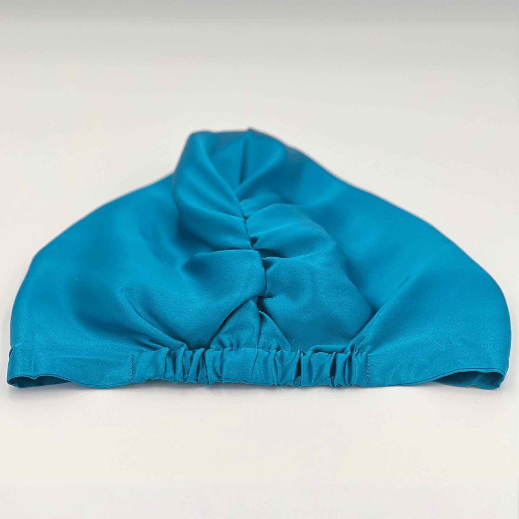 Back view of a teal silk bonnet laying flat