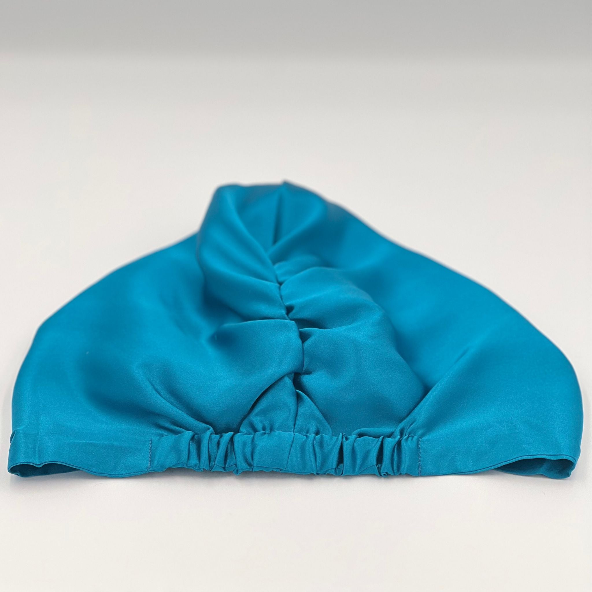 Back view of a teal silk bonnet laying flat