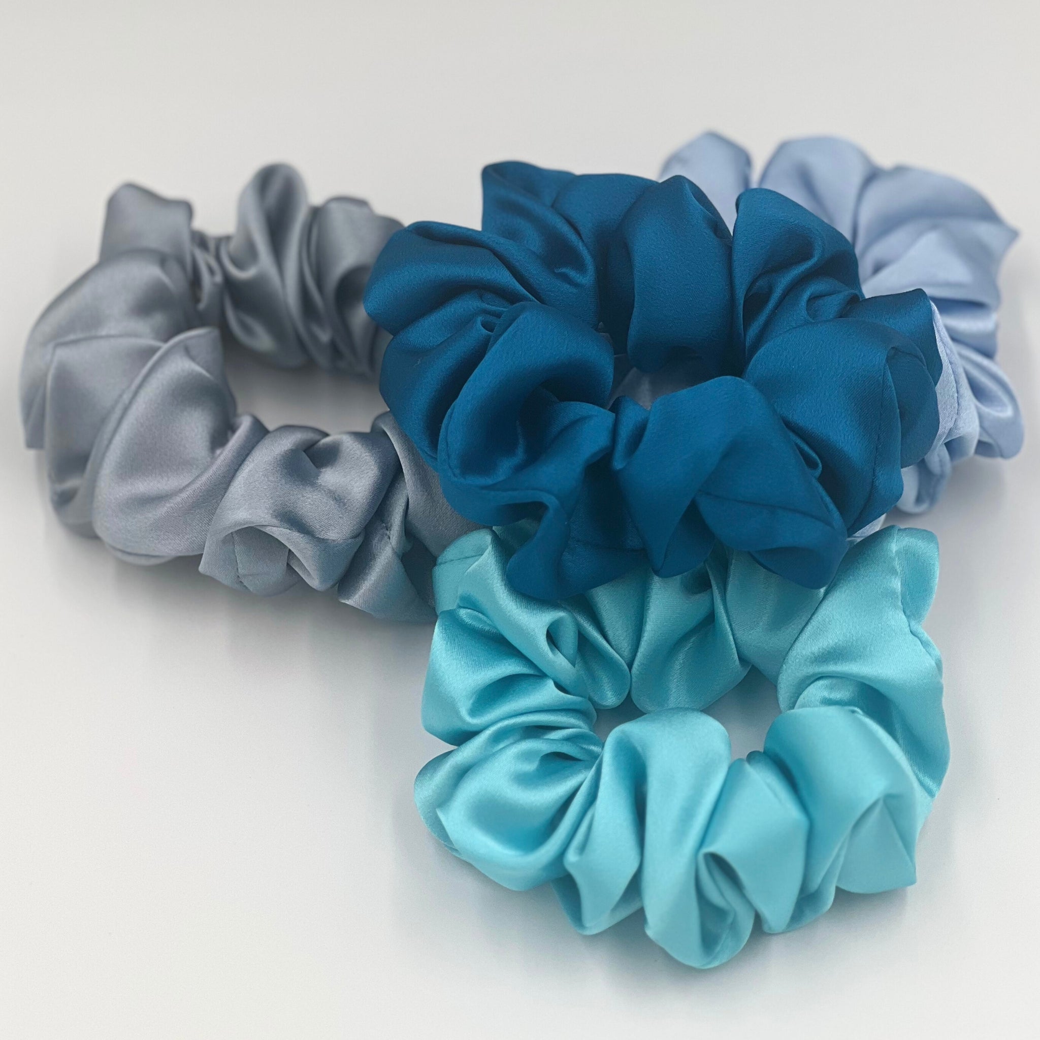 dusty blue, baby blue, robins egg blue and crystal teal silk scrunchies in a pile