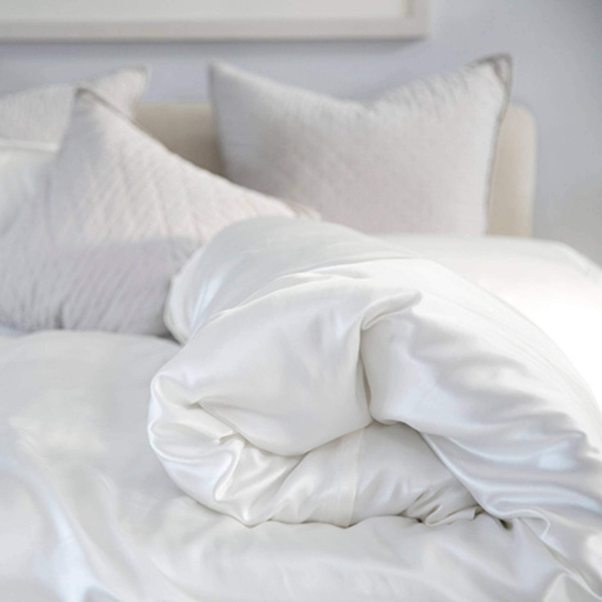 rolled up silk duvet cover on a bed with silk pillows and decorative pillows in the background