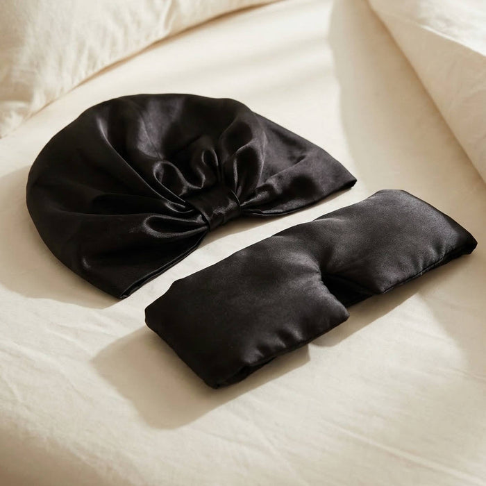 Black silk hair bonnet and eye mask on a beige surface