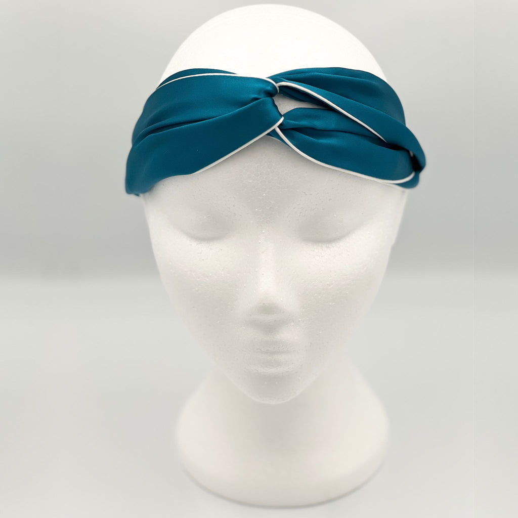 A teal silk headband on a mannequins head. The headband shows a tie front