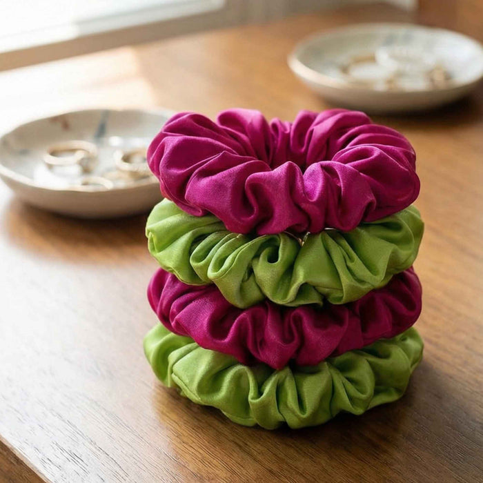 Stack of pink and green silk scrunchies on a wooden table.