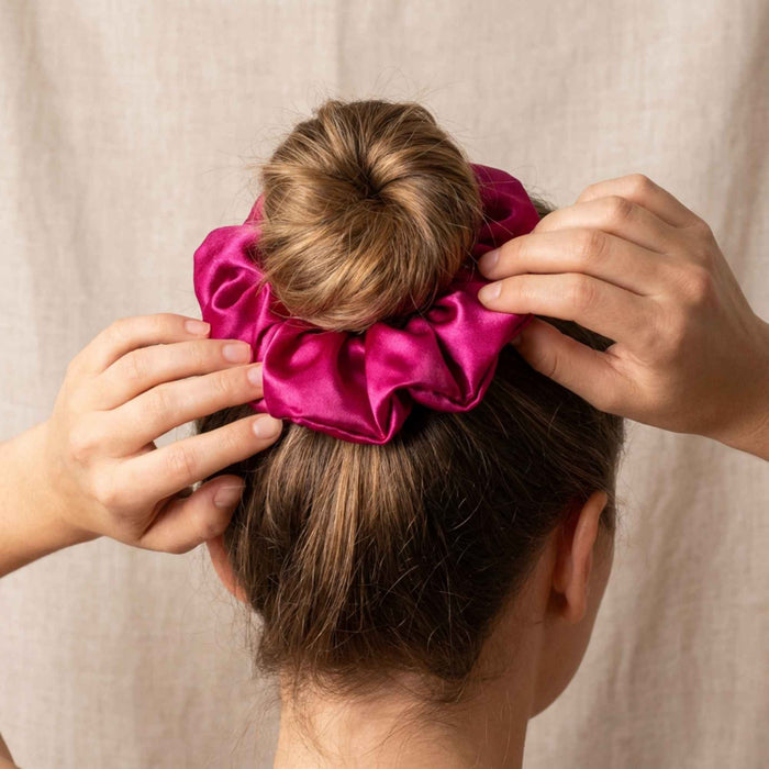 Person adjusting a pink silk scrunchie on their hair against a neutral background