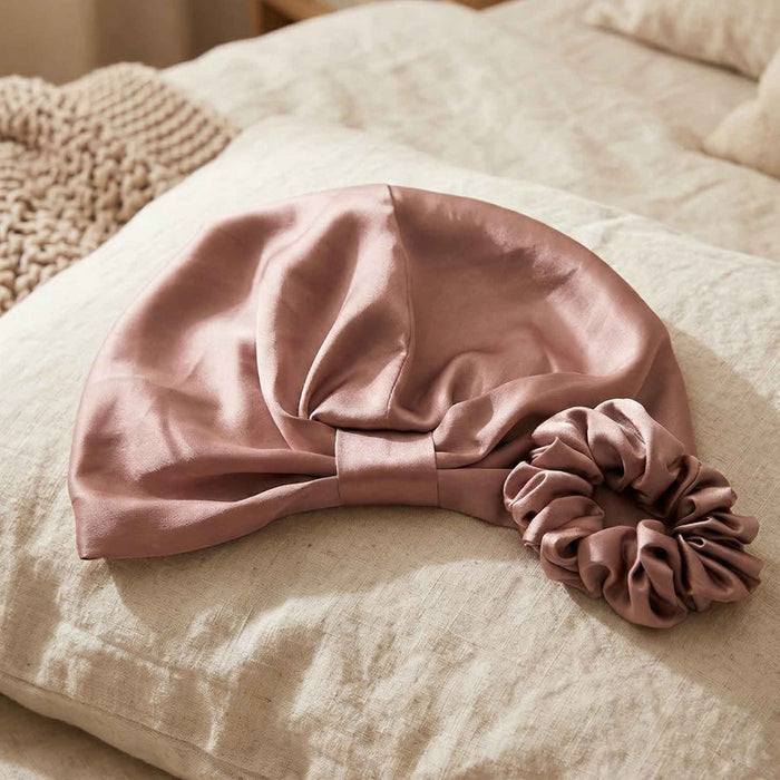 Pink silk hair bonnet and scrunchie on a textured surface