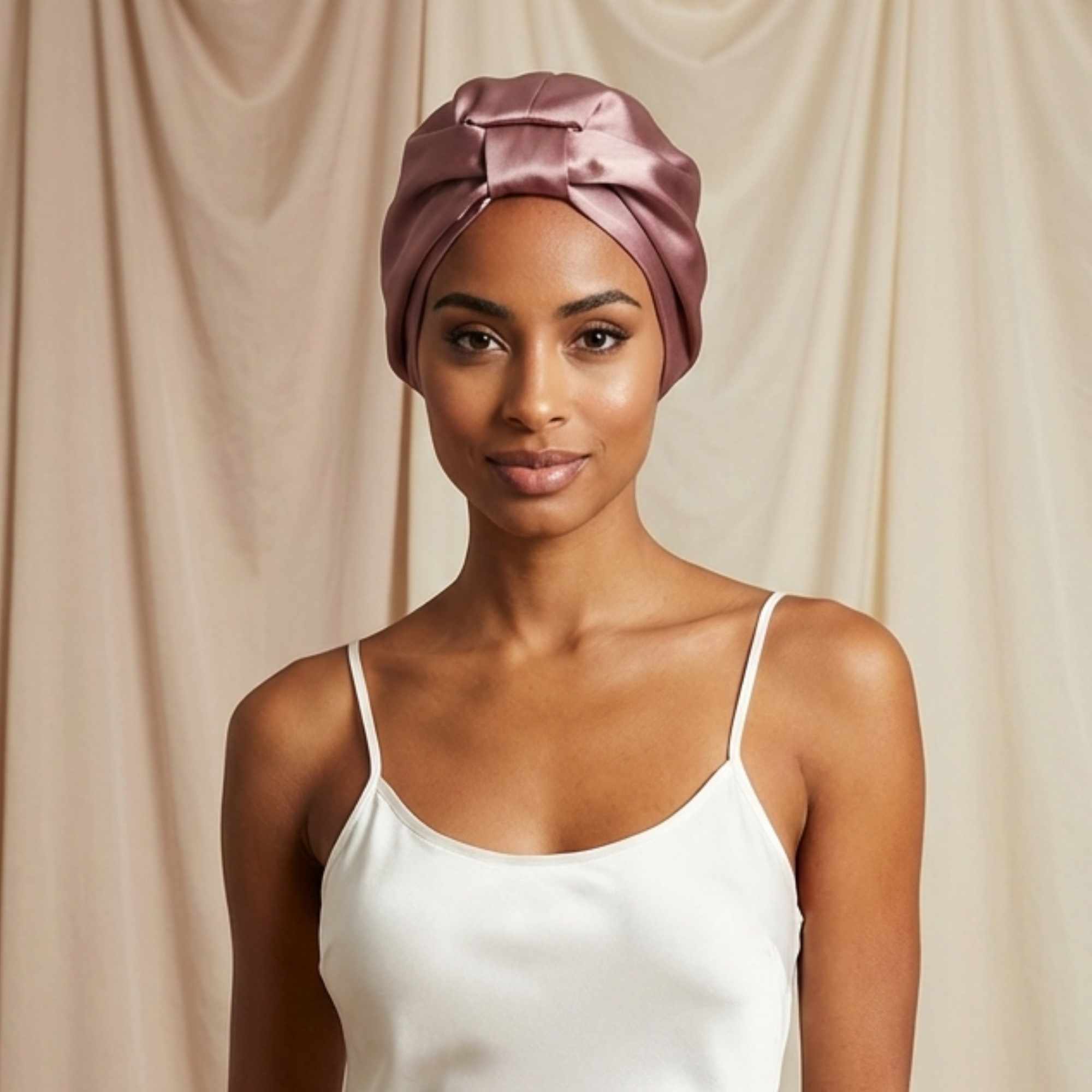 Woman wearing a dusty pink silk bonnet against a beige curtain background