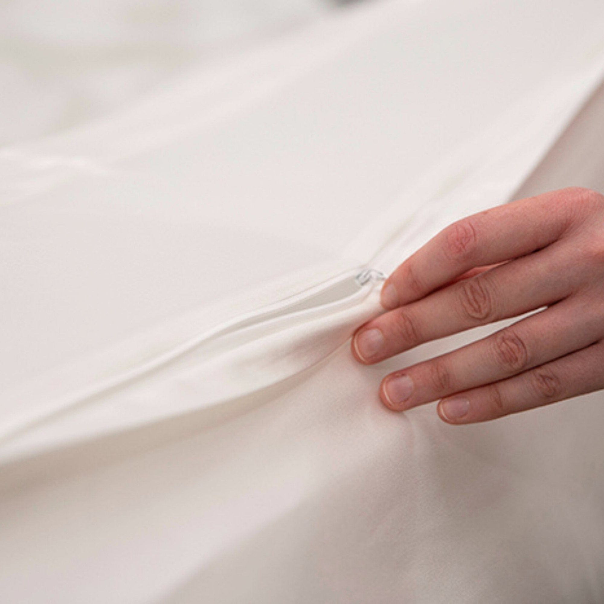 Close up of a hand using the concealed zip in an ivory silk duvet cover