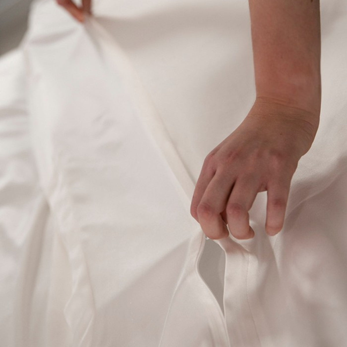 Close-up of a hand touching a smooth, ivory silk fabric surface with a concealed zip