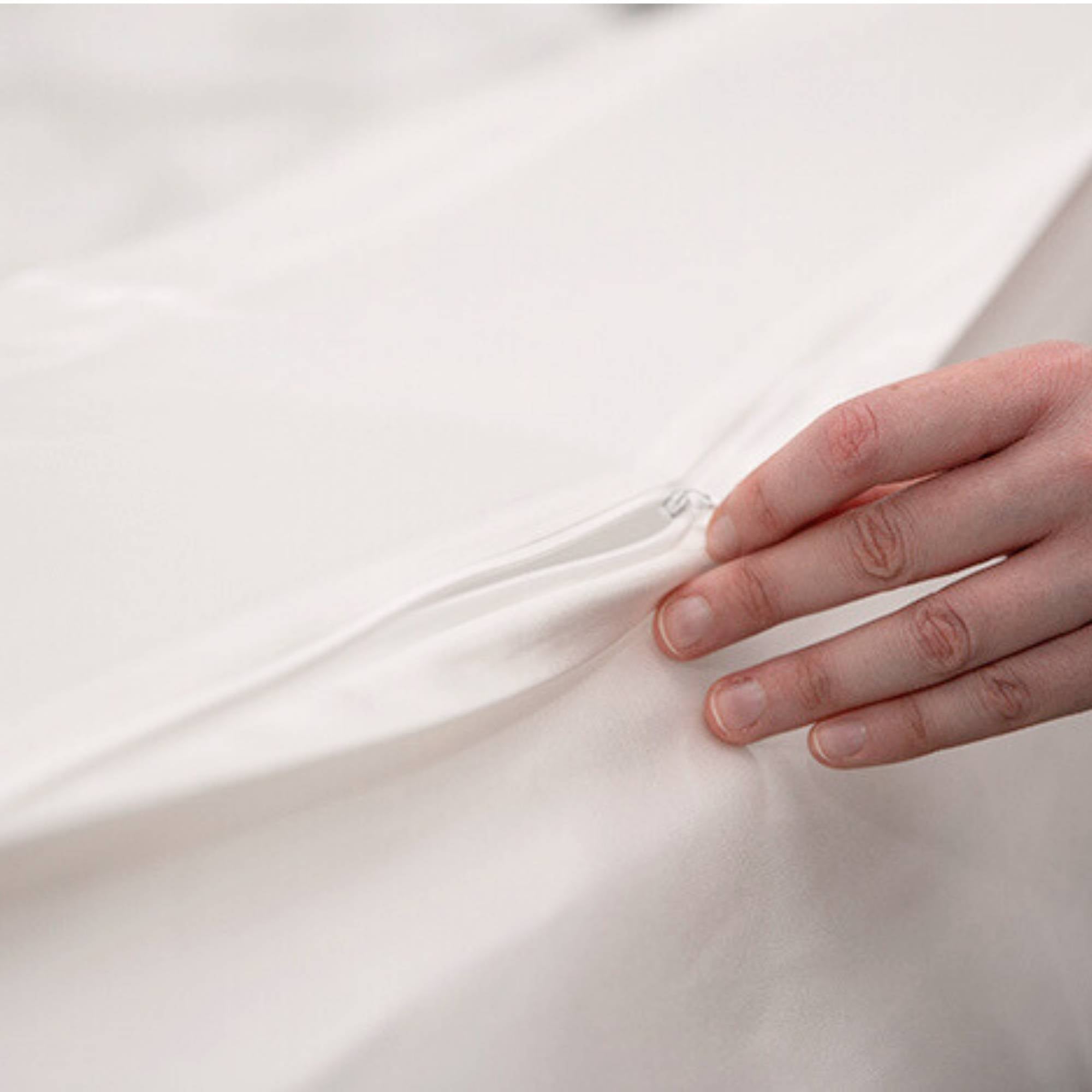 Close-up of a hand touching a smooth, ivory silk fabric surface with a concealed zip