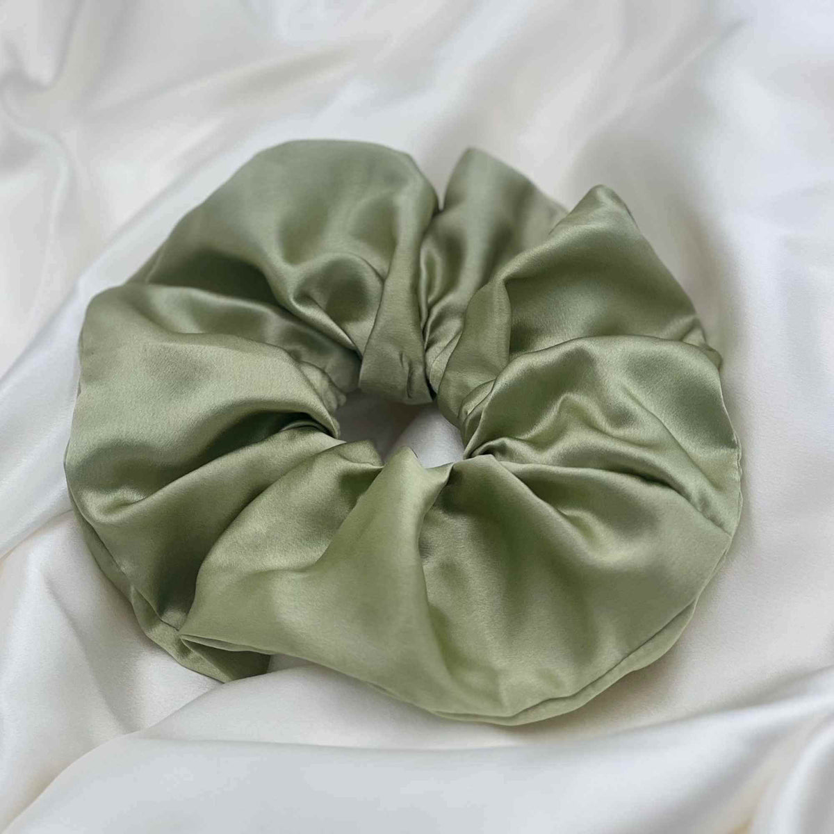 pistachio Green mulberry silk scrunchie on a white fabric background