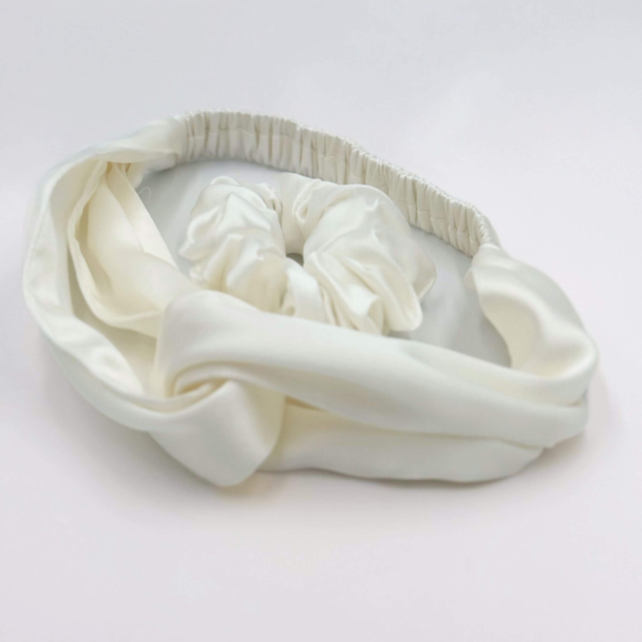 White silk headband with a textured band and a white silk scrunchie on a light gray background