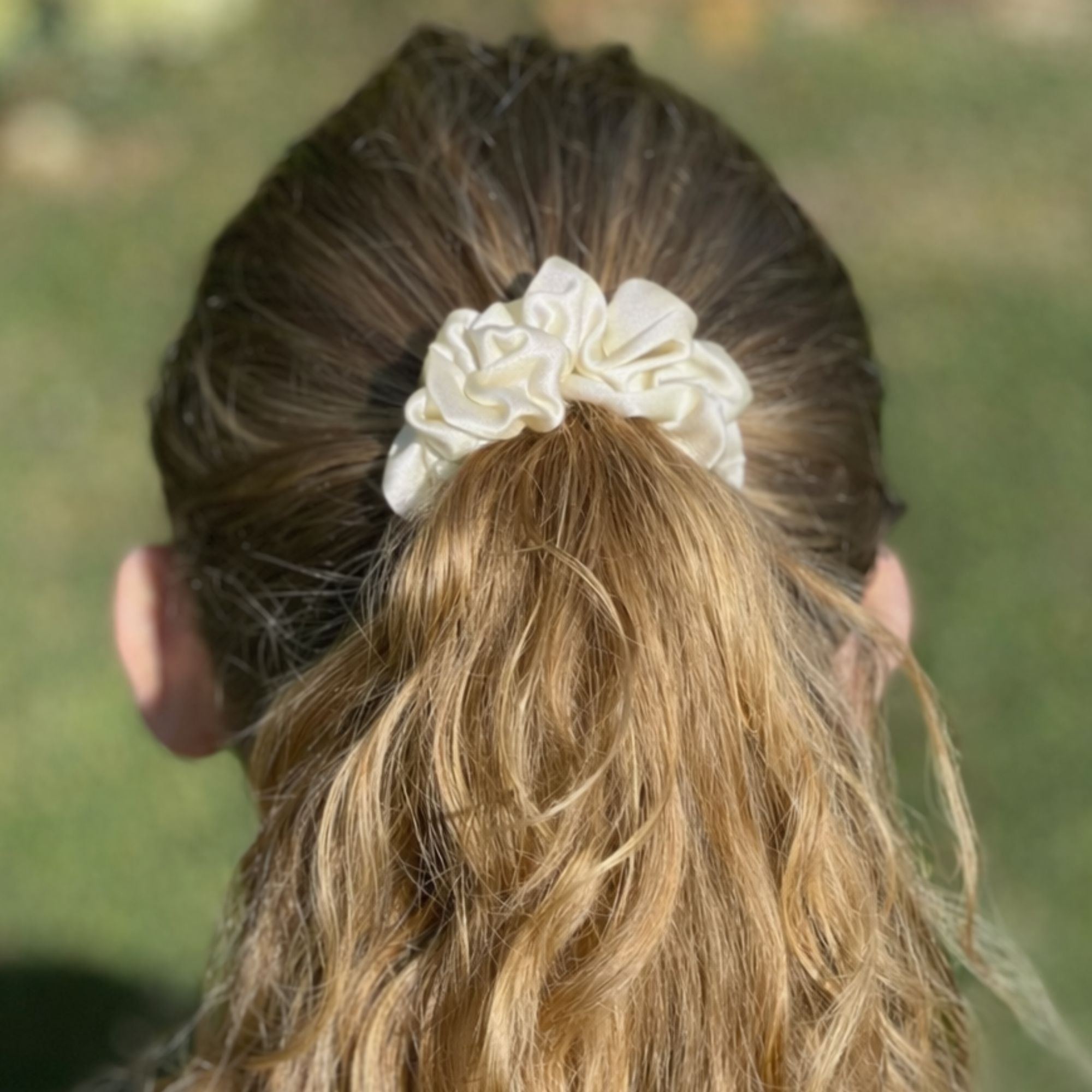 Person with an ivory white silk scrunchie in their hair against a blurred green background