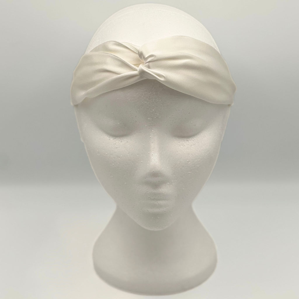 An ivory silk headband on a mannequins head. The front shows a tie 