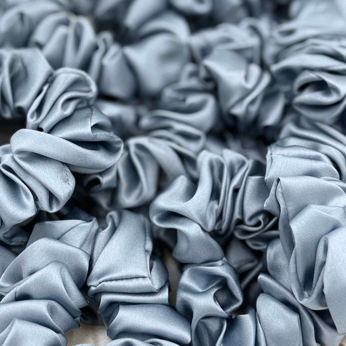 Multiple dusty blue mulberry silk scrunchies stacked together
