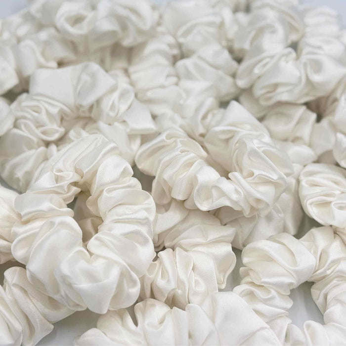 Close-up of multiple ivory white mulberry silk scrunchies on a white background