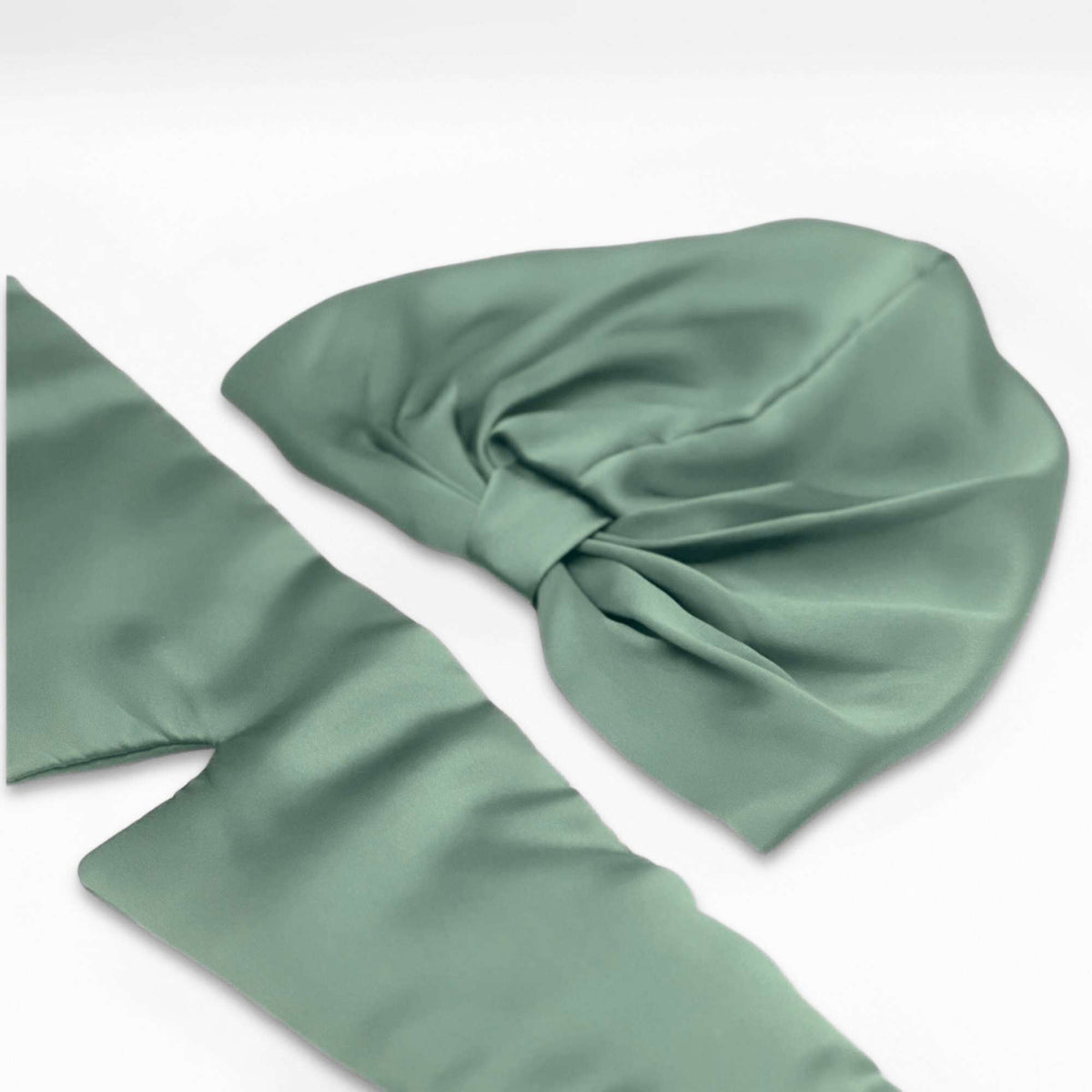 Green silk bonnet and eye mask set lying flat on a white background