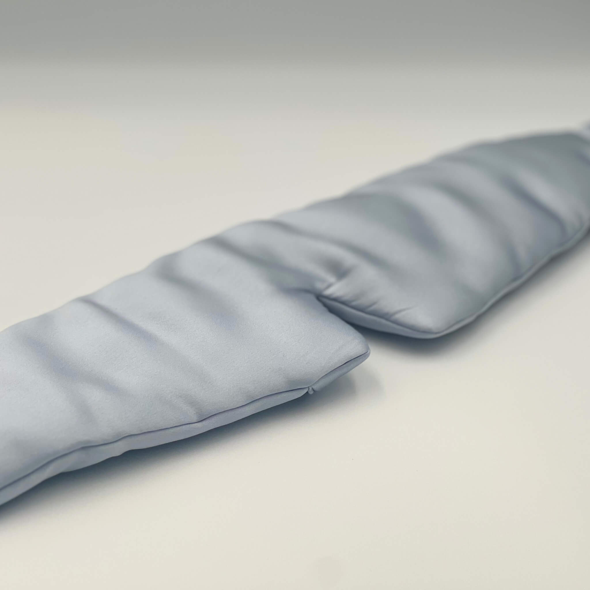 Pale blue silk eye mask lying flat on a white background
