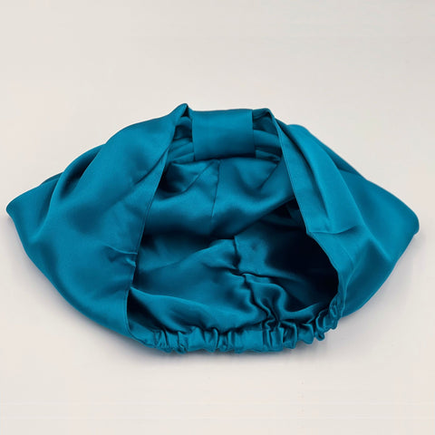 Teal bonnet laying flat, showing it's reversible quality, line with silk