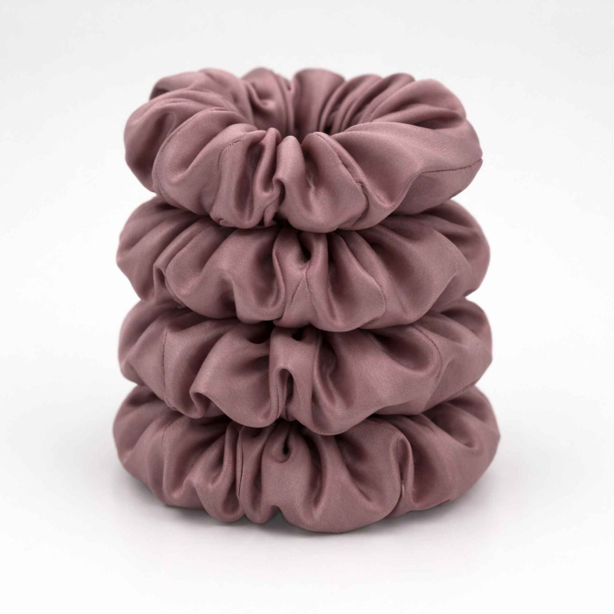 Stack of four dusty pink silk scrunchies on a white background