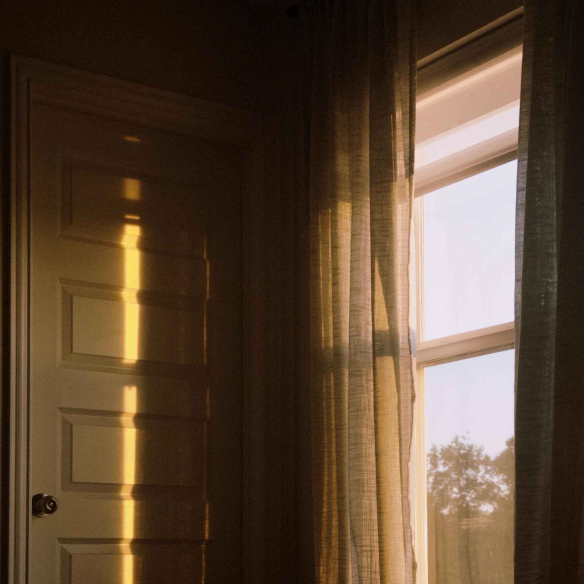 Sunlight filtering through curtains on a window with a door in the background