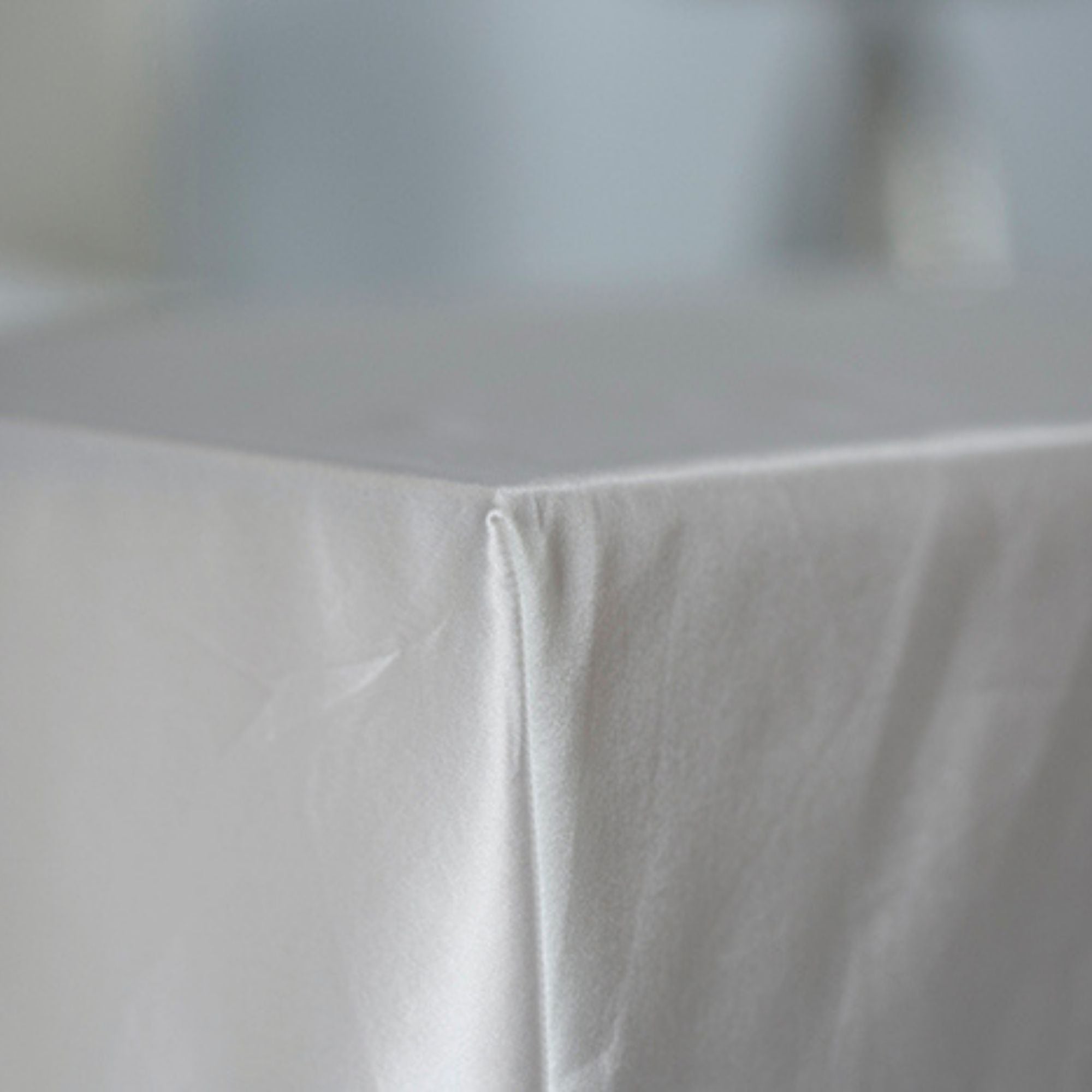Close-up of an ivory silk fitted sheet tailored corner with a blurred background