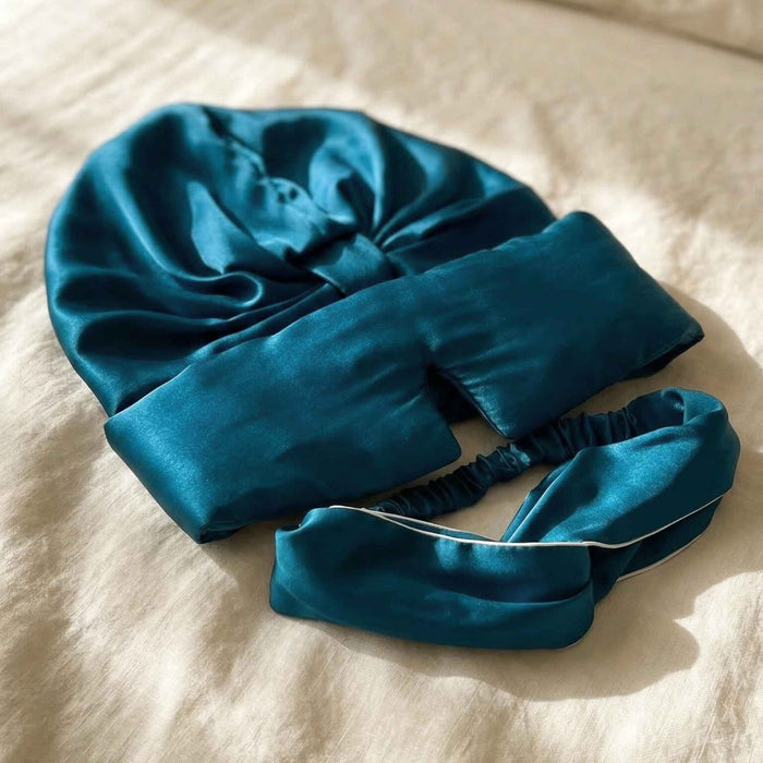 Blue silk hair bonnet, eye mask and headband on a beige surface