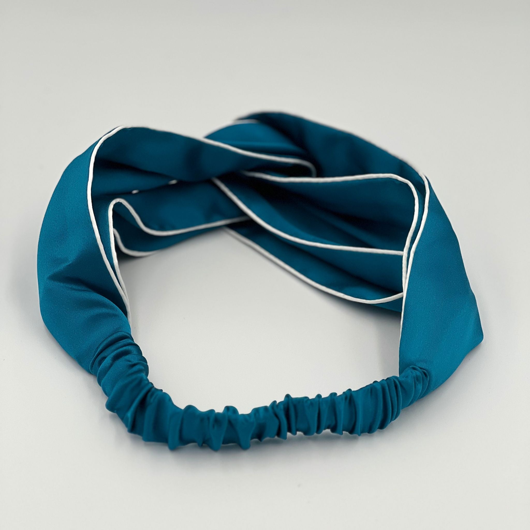 The back of a teal silk headband lying flat